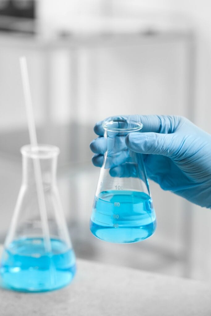 glass flask in chemistry with hand in a blue glove holding the flask